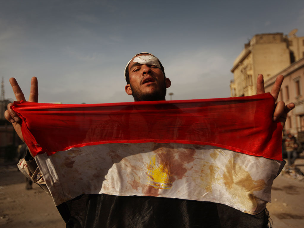 An anti-government protestor holds a blooded Egyptian flag in Tahrir Square in Cairo