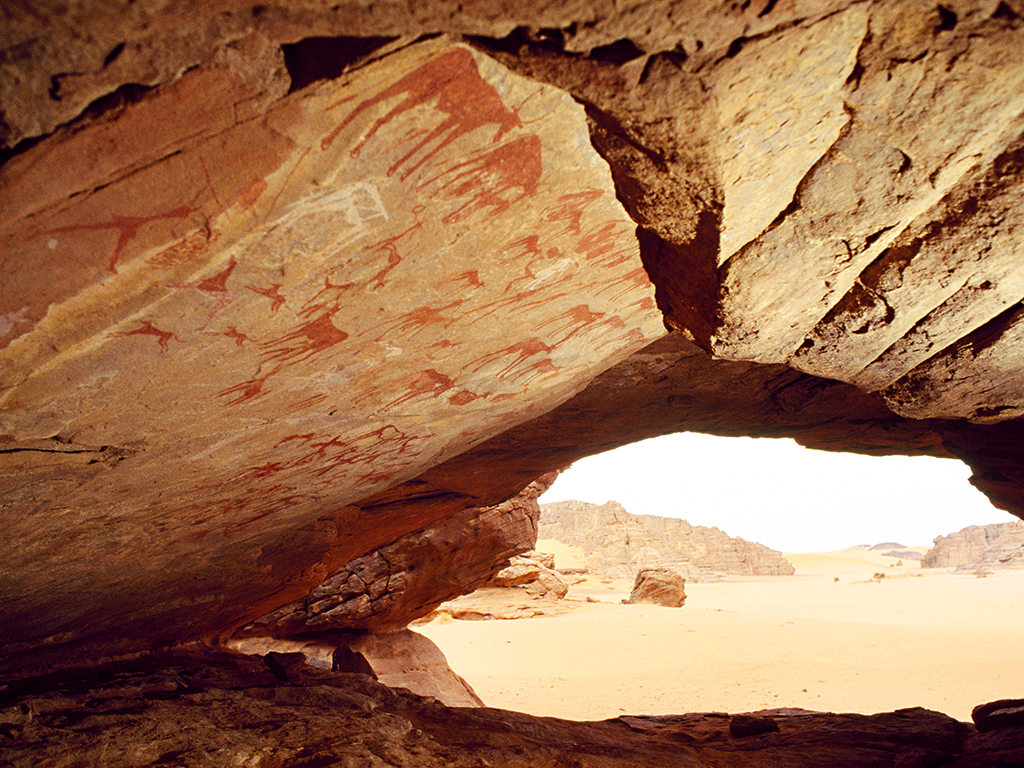 Looking out of a low cave in southern Algeria over a riverbed whose waters may not have flowed for several thousand years. Its roof is decorated with pastoral paintings made when the Sahara was green