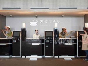 A guest is greeted at the front desk of Henn-na Hotel by a Japanese-speaking humanoid and an English-speaking Velociraptor robot